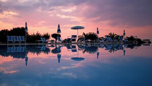 A poolside area with lounge chairs and umbrellas, surrounded by palm trees and a clear sky at sunset. - Agriresidence Ninea (Ricadi)