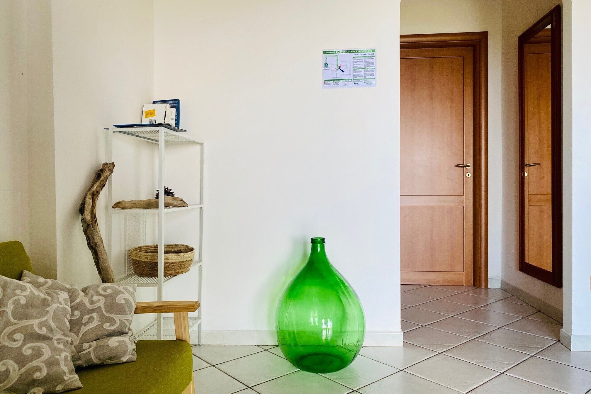Ein Wohnzimmer mit einer grünen Vase, einer Holztür und einer weißen Wand mit einem kleinen Notausgangsschild.