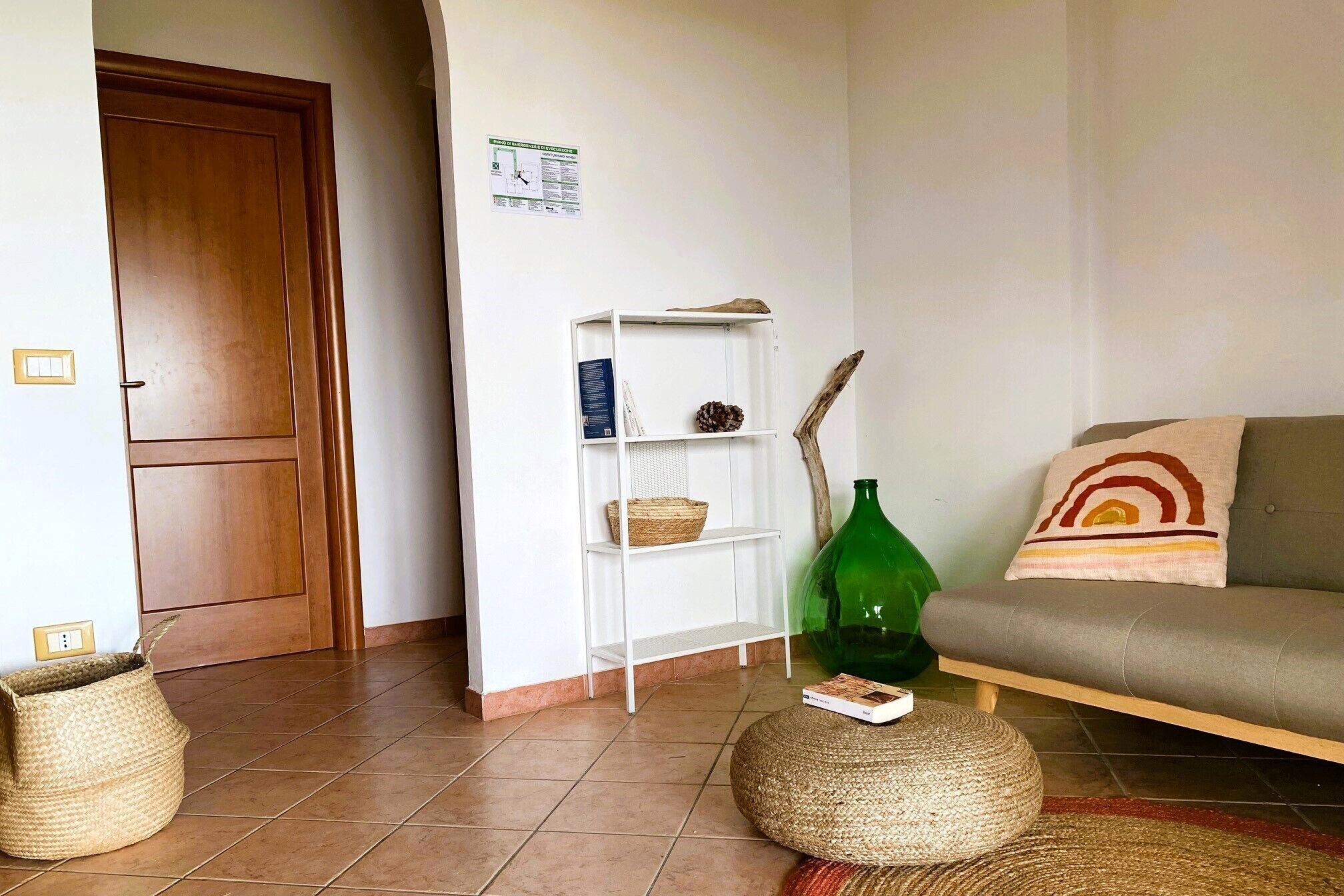 A living room with a sofa, a green vase, and a woven pouf.