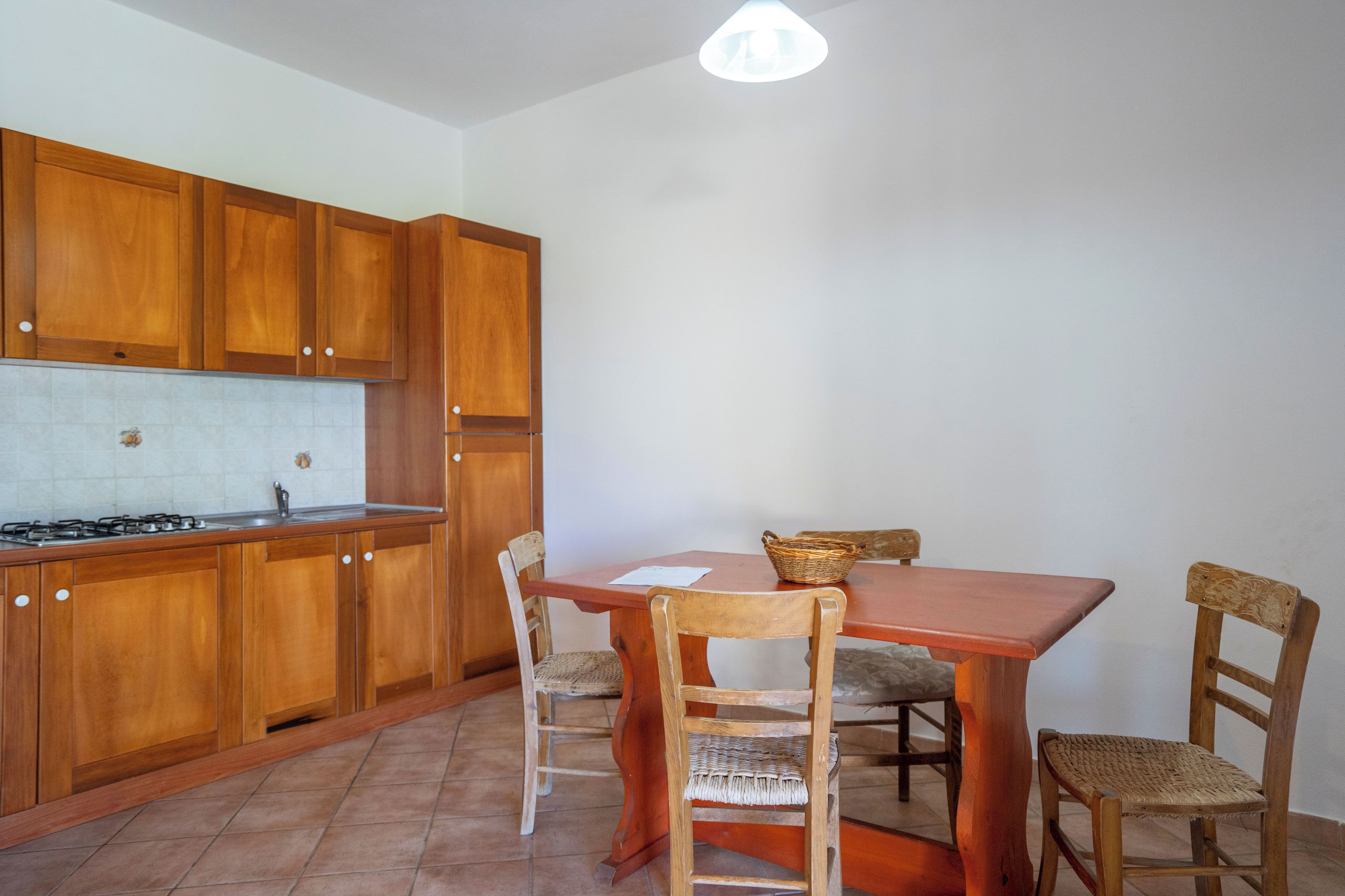 Une cuisine avec des meubles de rangement en bois, une table à manger avec des chaises et un luminaire suspendu.