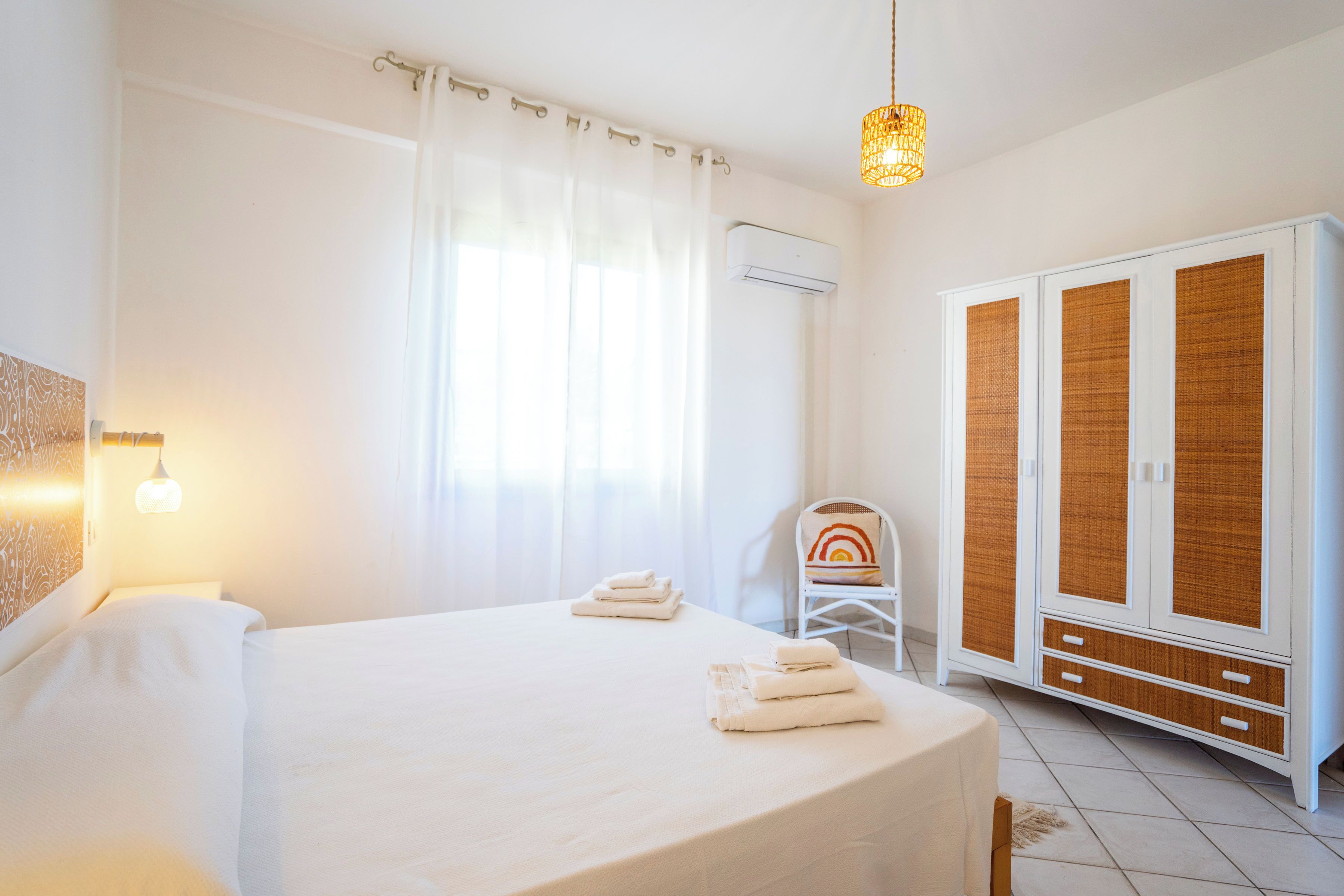 A bedroom with a bed, a chair, a wardrobe, and a hanging light fixture.