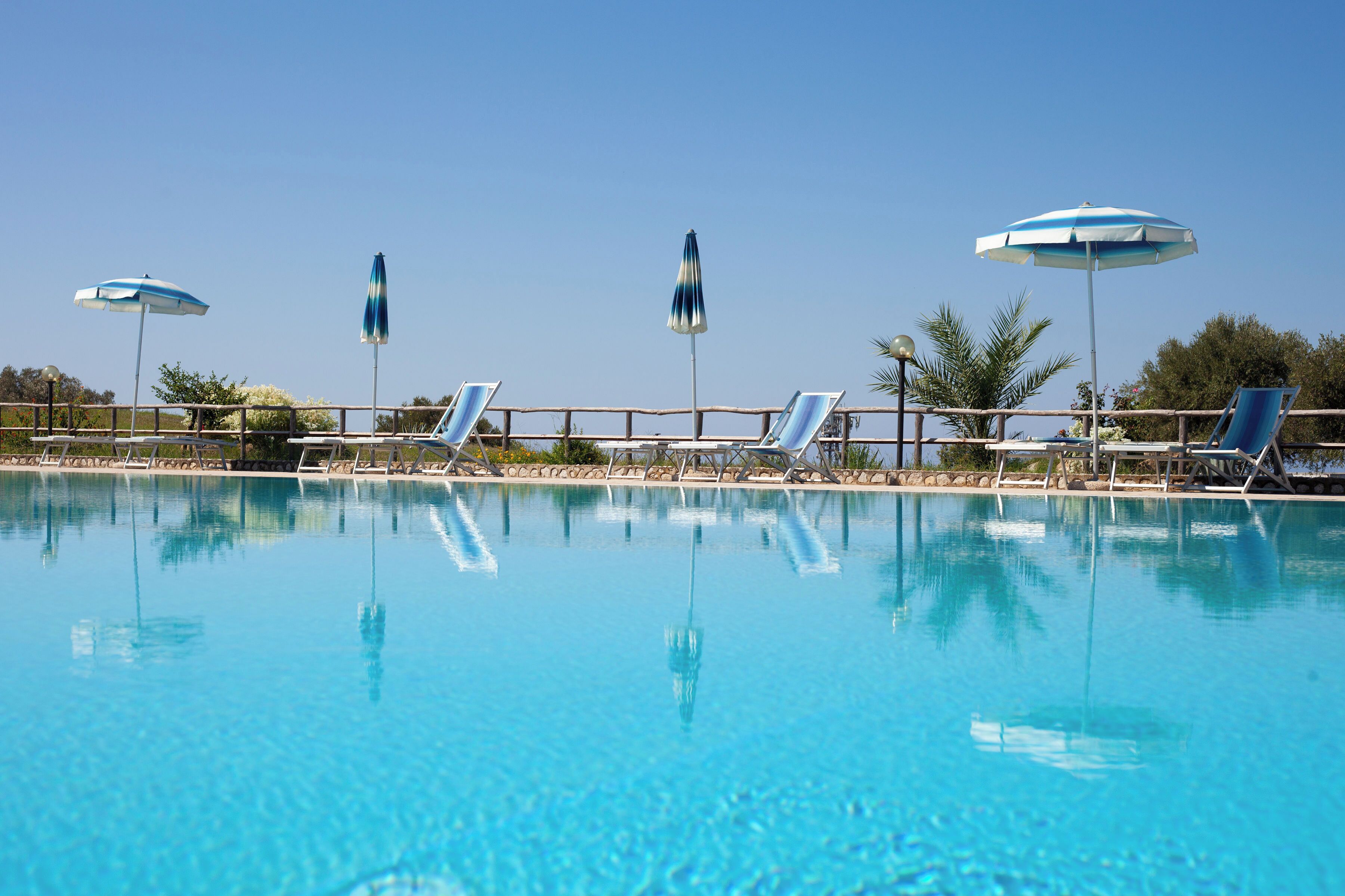 A clear swimming pool with lounge chairs and umbrellas.