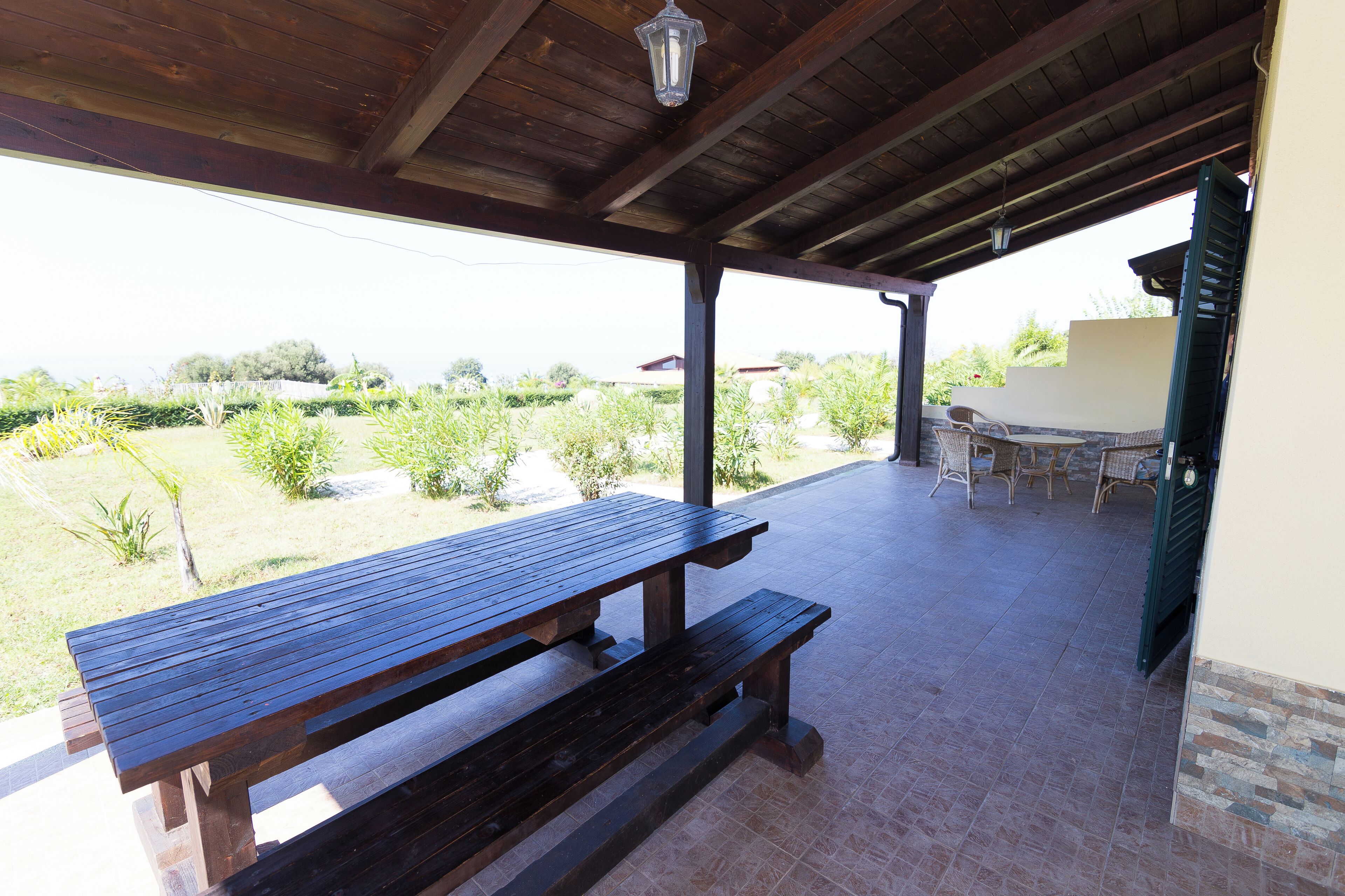 A wooden picnic table with benches under a covered patio area.