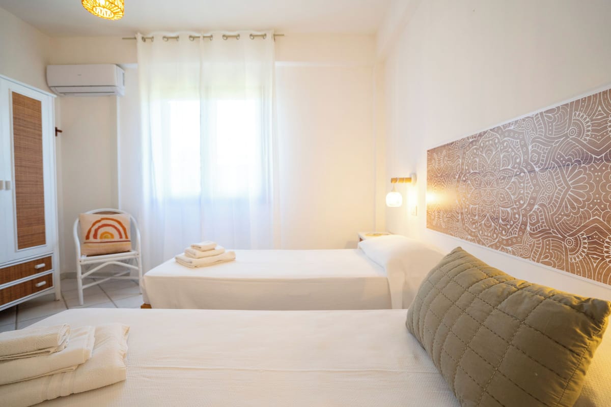 Hotellihuone, jossa on sänky, tuoli, pyyhkeillä varustettu pöytä, ilmastointilaite ja kuvioitu seinä.