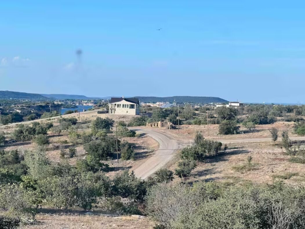 Paisaje rural con un edificio en una colina, rodeado de vegetación escasa y cielo despejado.