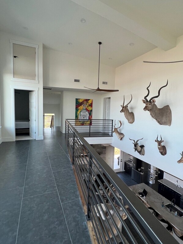 A spacious living area with a high ceiling, a modern kitchen, and a staircase leading to an upper level. - POSSUM KINGDOM LODGE: AMAZING LUXURY HOME --- HELL' S GATE (Strawn)