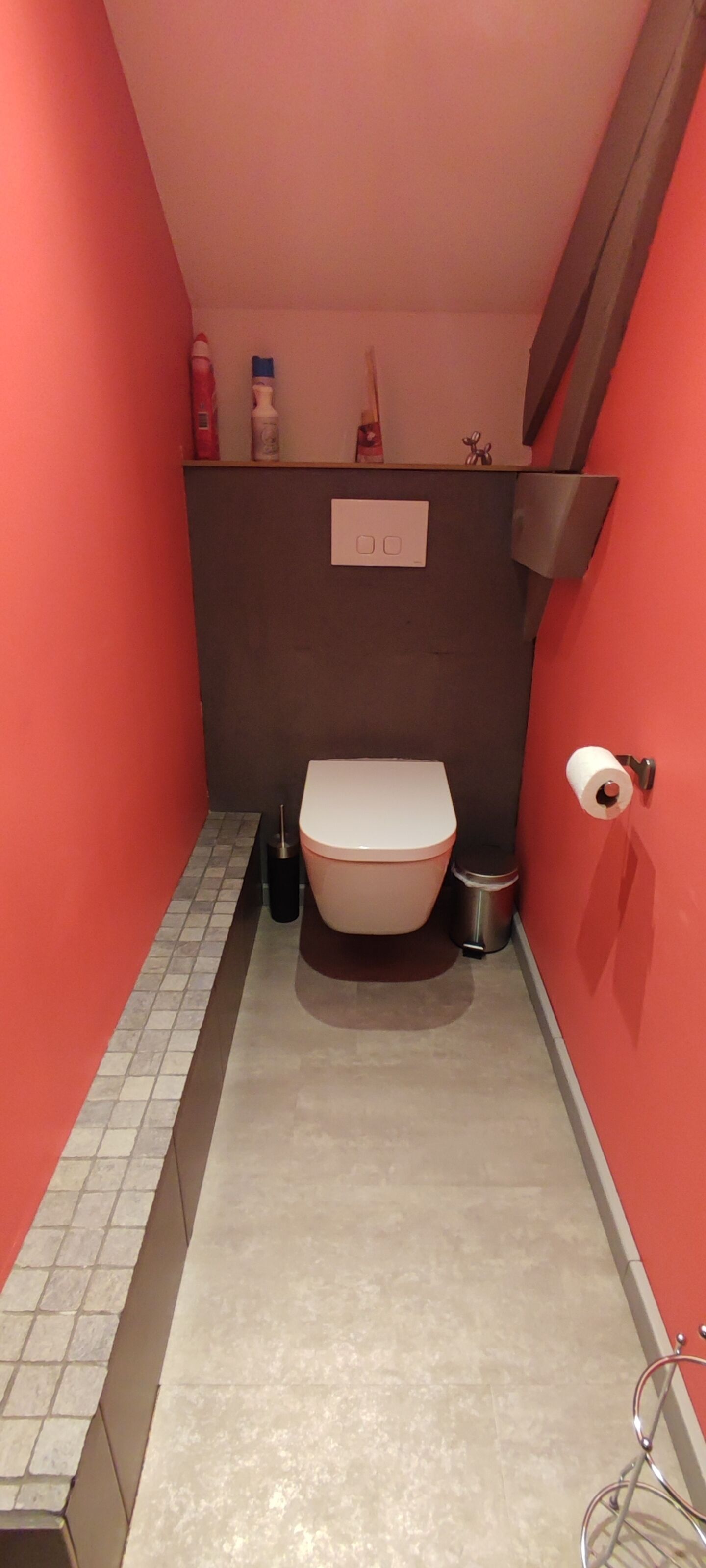 Ein schmales Badezimmer mit Toilette, Mülleimer und Toilettenpapierhalter.