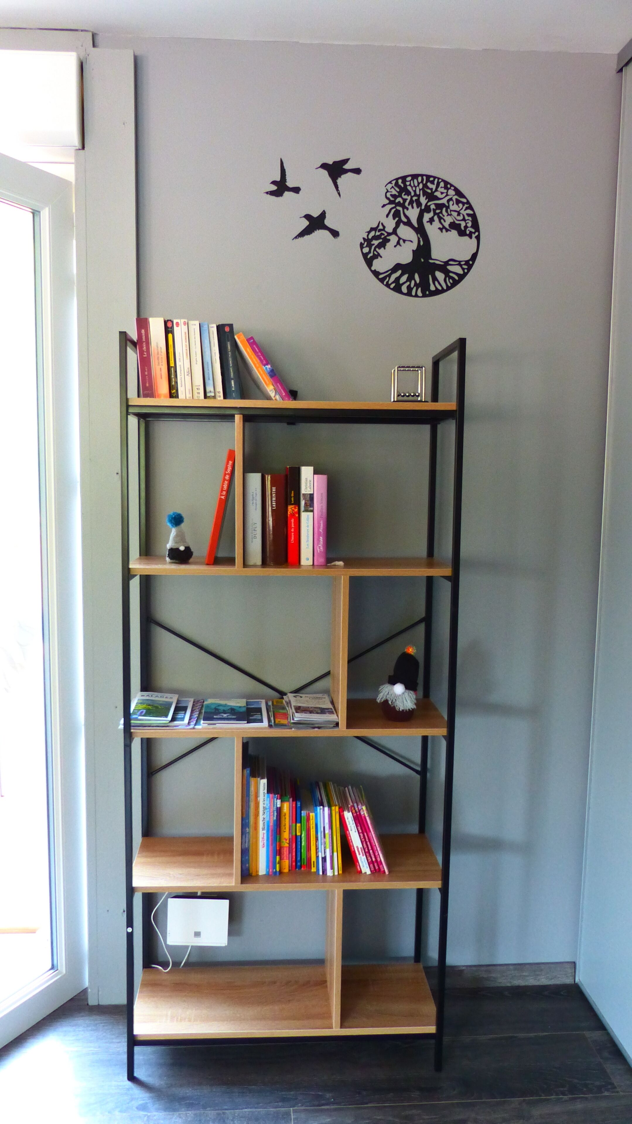A bookshelf with books and decorative items against a wall with a tree decal and flying birds decal.