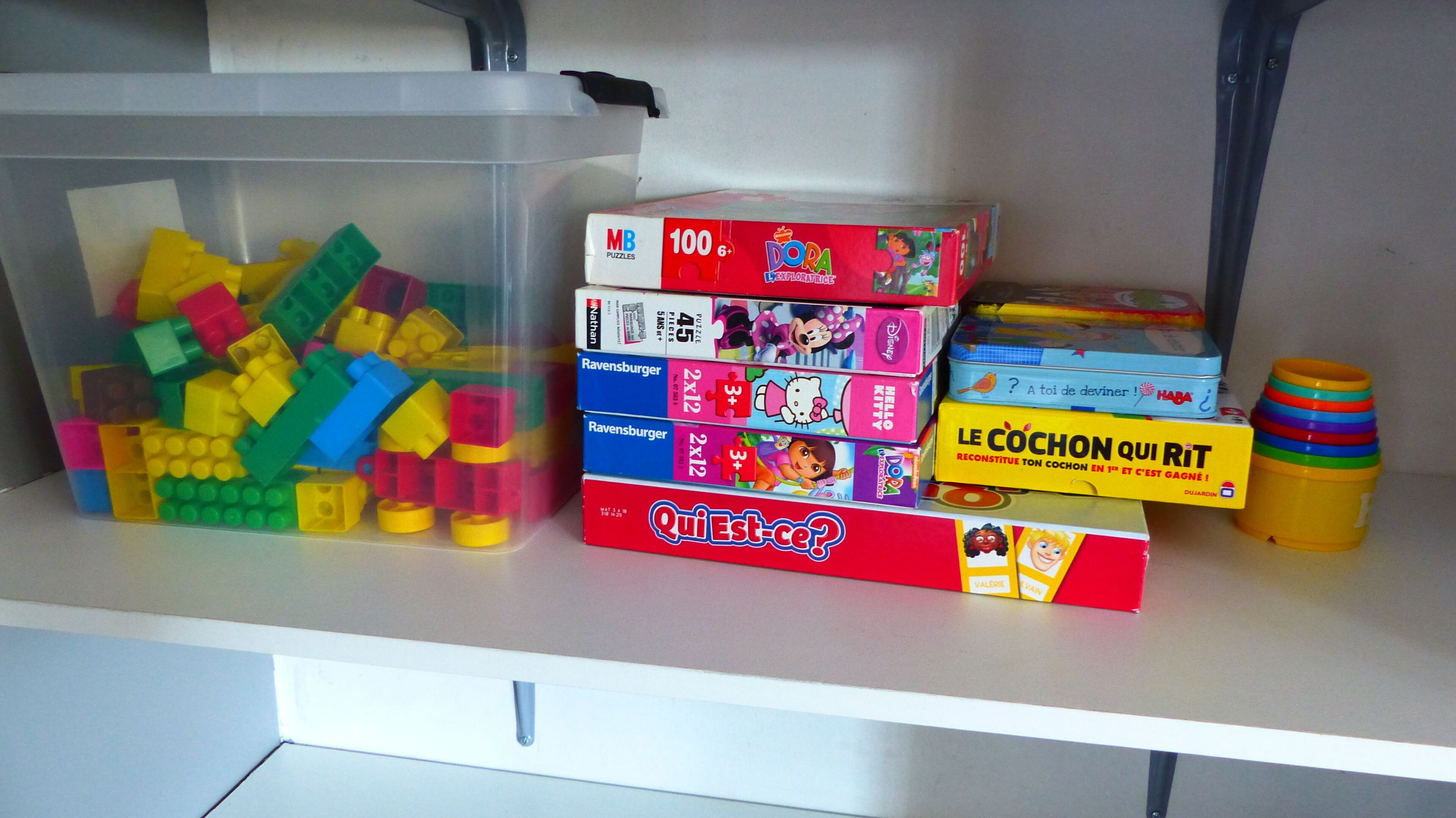 A storage area with various children's toys and puzzles, including a large container of building blocks and several boxed games.