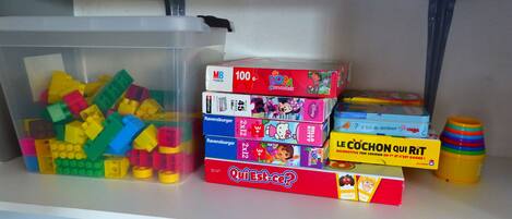 A storage area with various children's toys and puzzles, including a large container of building blocks and several boxed games.