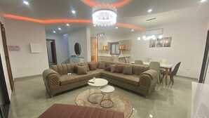Moderni olohuone, jossa on kulmasohva, ruokapöytä ja kattokruunu.