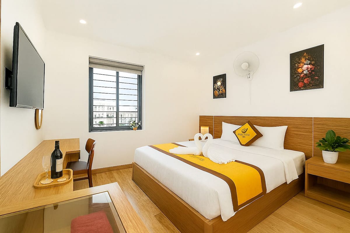 Habitación de hotel con cama, escritorio, silla, televisor, ventana y una planta.