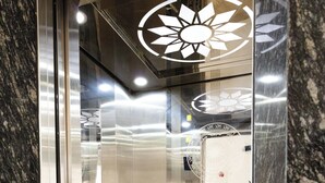 Interior de un ascensor con piso de mármol, paredes metálicas y un panel de control con botones.