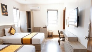 Habitación de hotel con dos camas, un escritorio, una silla y un televisor en la pared.