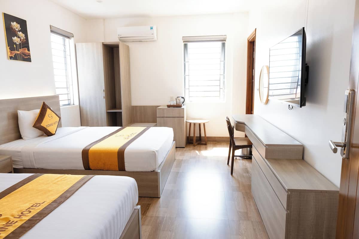 Habitación de hotel con dos camas, un escritorio, una silla y un televisor en la pared.