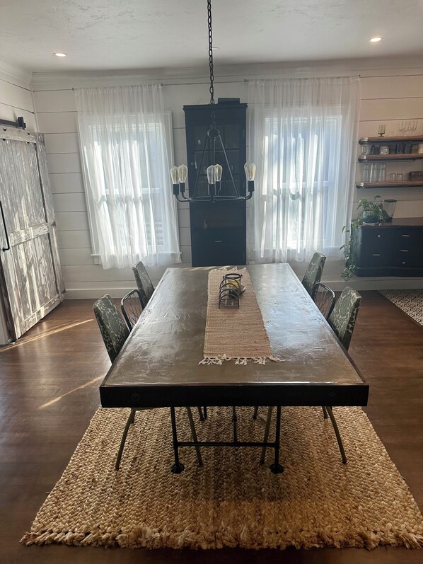 Ein Essbereich mit einem langen Tisch, Stühlen, einer Chandelüster und einem Teppich.