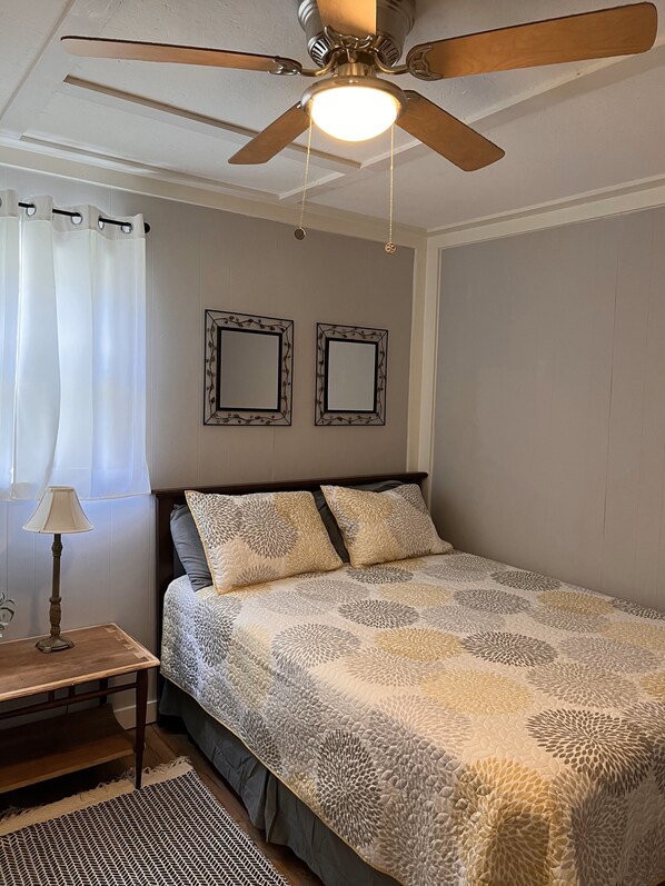 A bedroom with a bed, a ceiling fan, two wall mirrors, a bedside table with a lamp, and a patterned rug. - Cozy cabin with riverfront location, fire pit and peaceful surroundings (Ellijay)