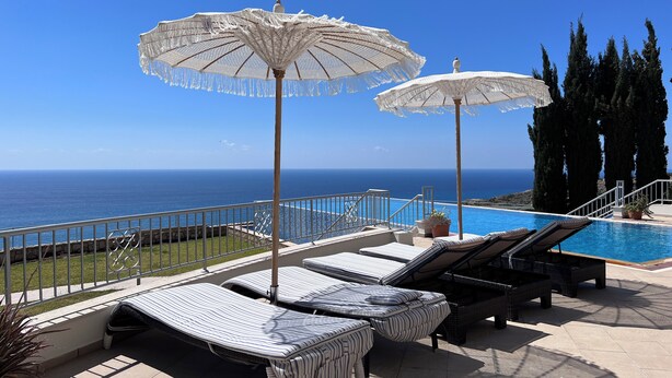 A poolside area with lounge chairs and umbrellas, overlooking a clear blue sea. - Matteo Villa Limassol Cyprus (Limassol)