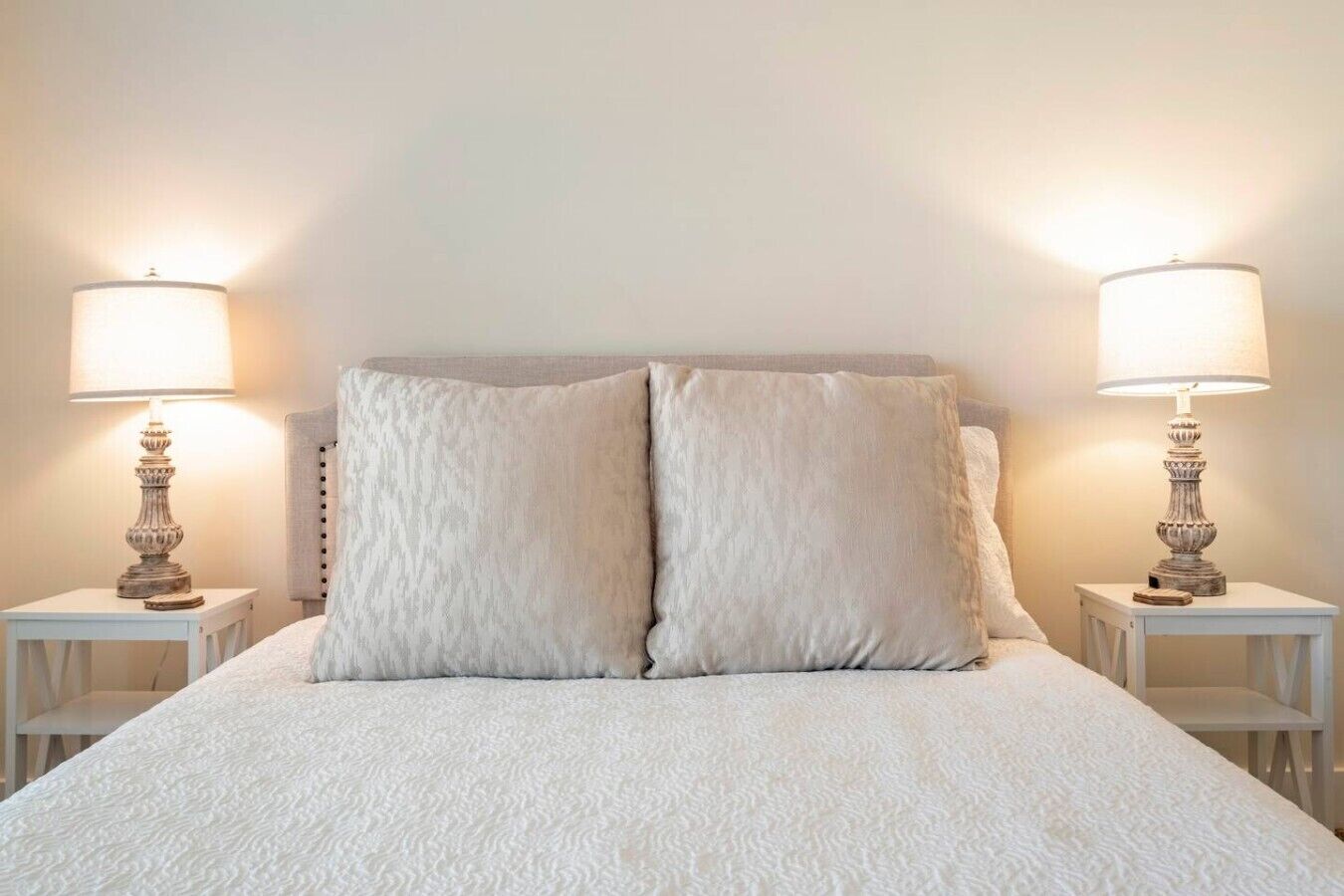 A bed with a textured white duvet, two matching pillows, and two bedside tables with lamps.