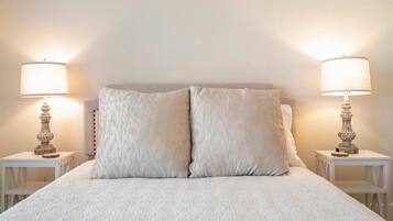 A bed with a textured white duvet, two matching pillows, and two bedside tables with lamps.