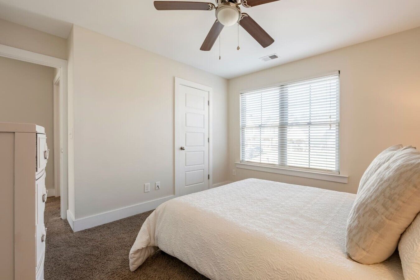 A bedroom with a bed, a ceiling fan, a door, and a window with blinds.