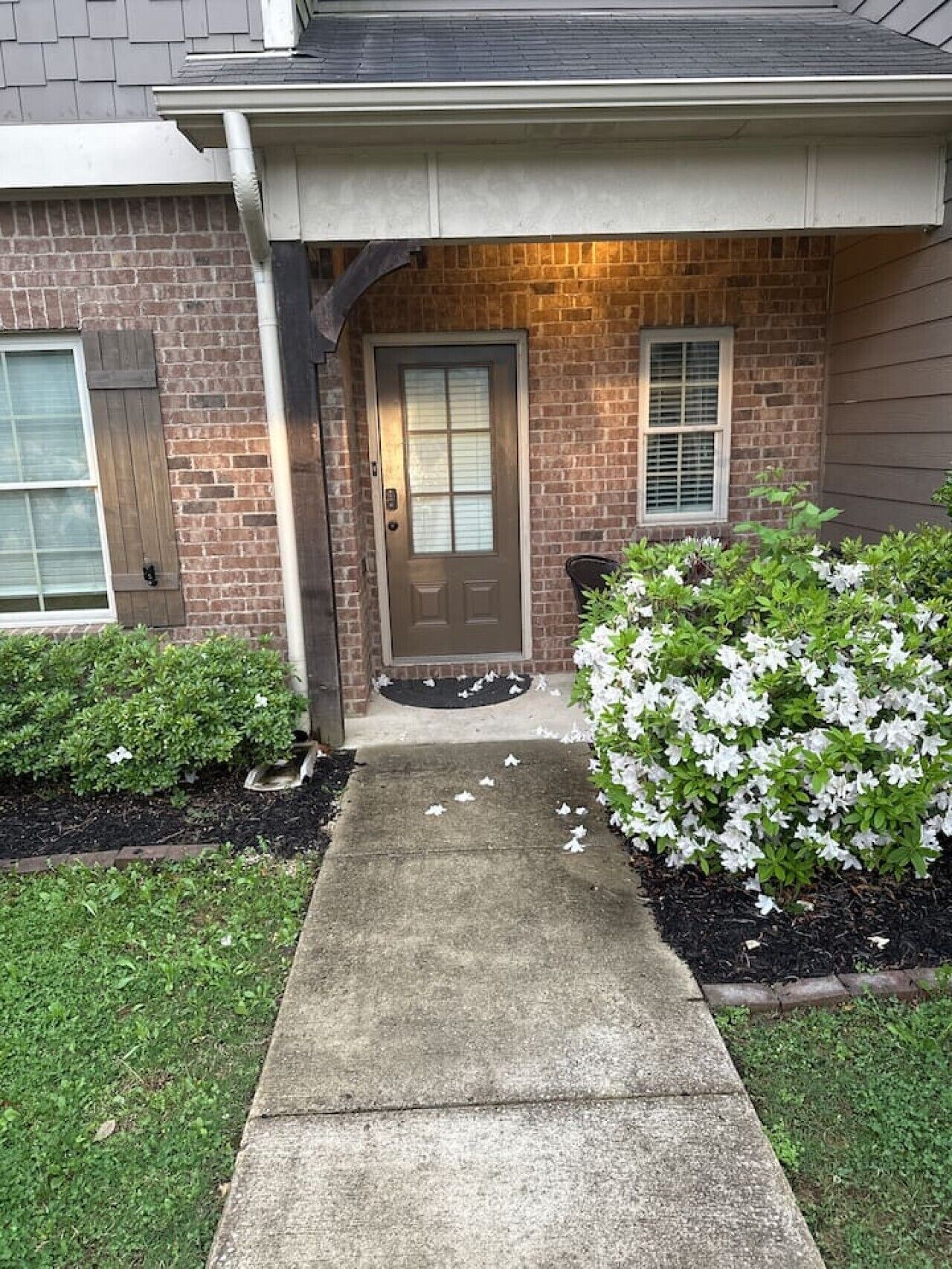 A residential house with a front door, a small porch, and a garden with white flowers.