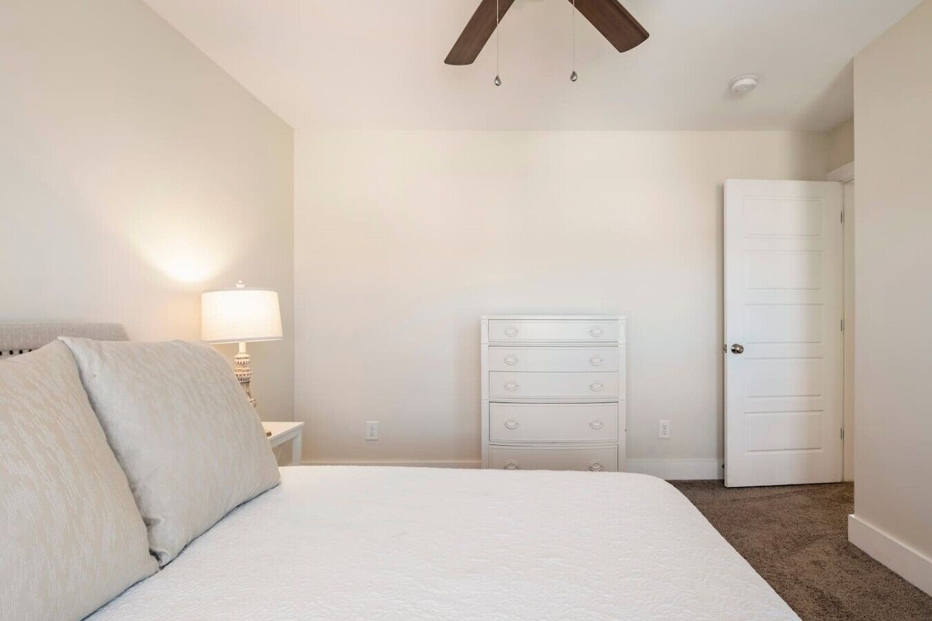 A bedroom with a bed, a dresser, a nightstand, a lamp, and a door.