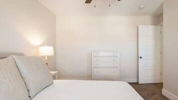 A bedroom with a bed, a dresser, a nightstand, a lamp, and a door.