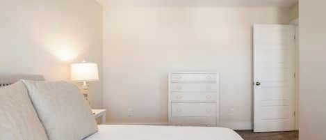 A bedroom with a bed, a dresser, a nightstand, a lamp, and a door.
