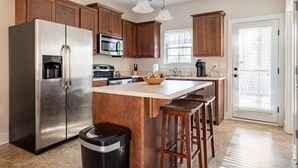 A kitchen with wooden cabinets, stainless steel appliances, a central island with stools, and a window with blinds. - Beautiful Home in the Heart of Hoover! (Hoover)