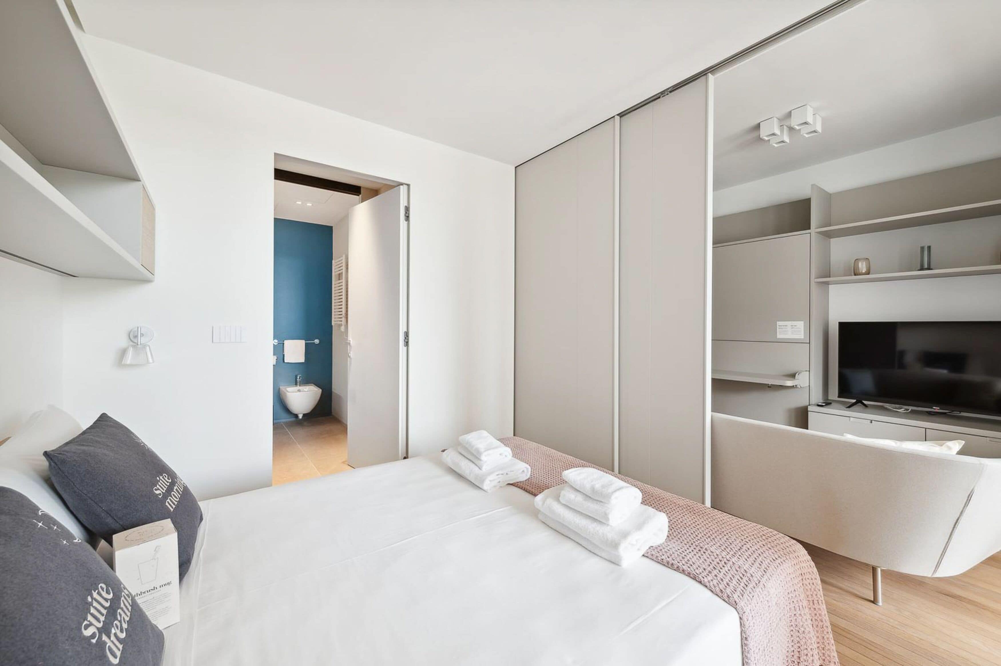 A modern hotel room with a large bed, a TV, and a walk-in closet.
