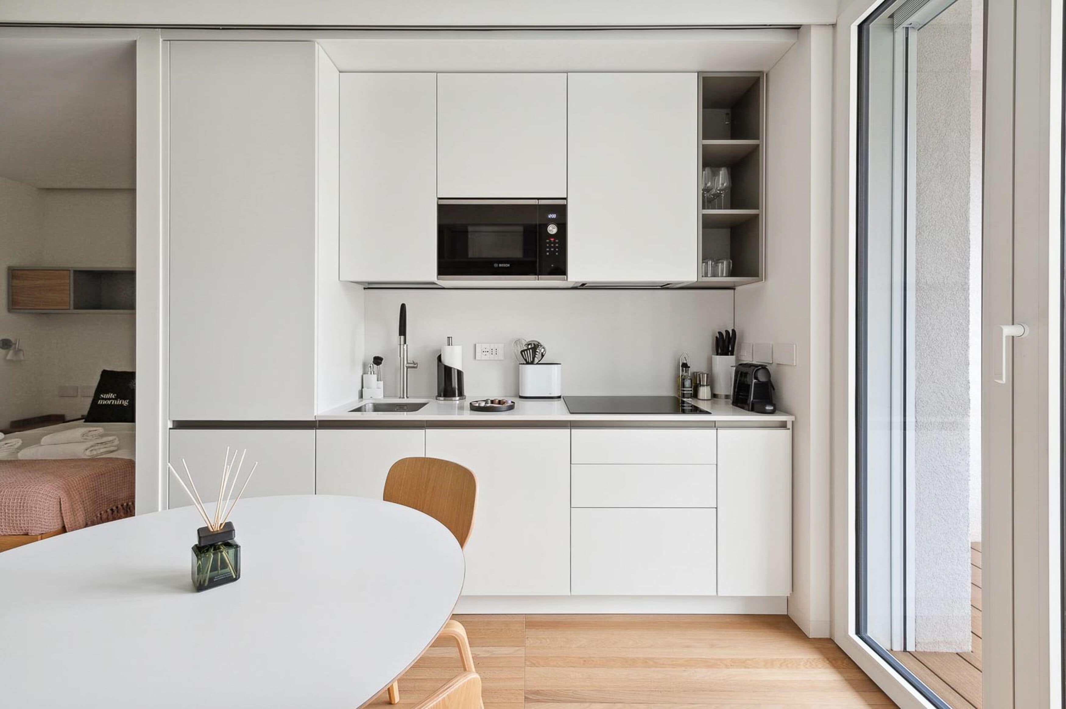 A modern kitchen with white cabinetry, a built-in microwave, and a coffee machine.