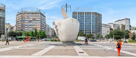 A large public square with a prominent sculpture in the center, surrounded by modern buildings and a clear sky.
