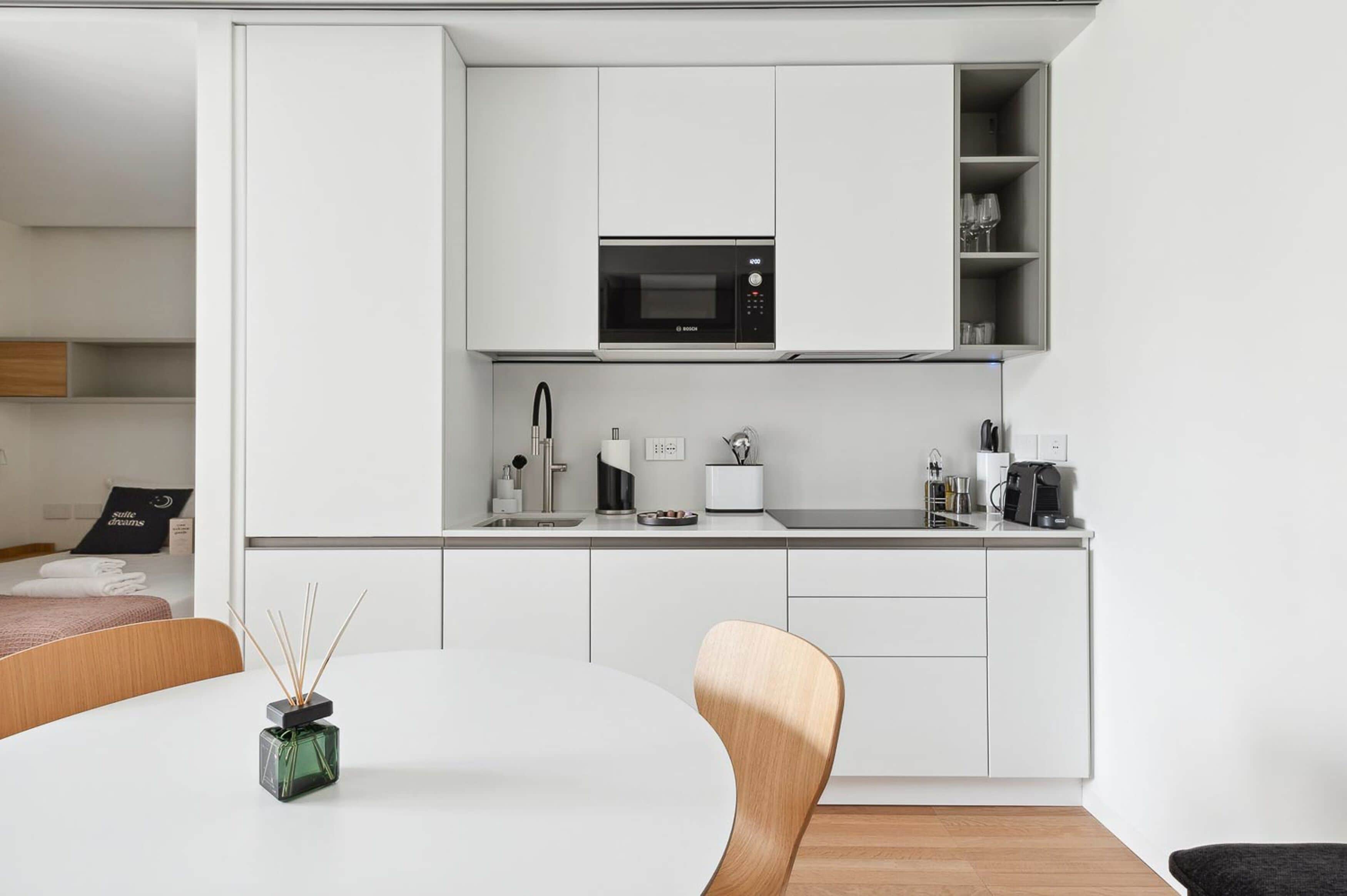 A modern kitchen with white cabinetry, a built-in microwave, and a coffee maker.