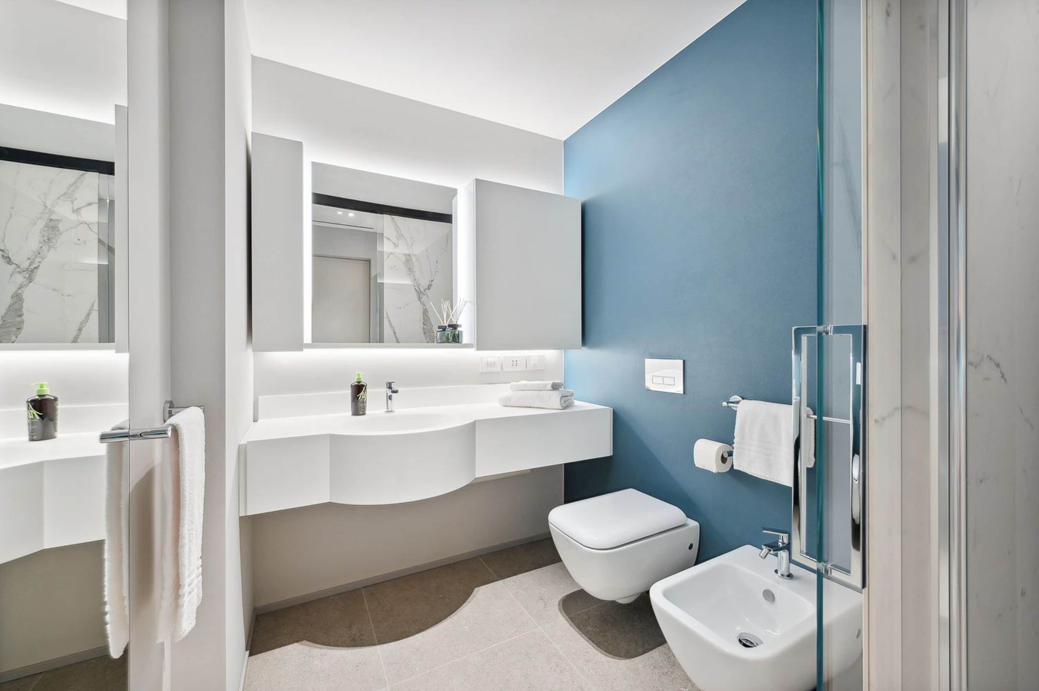 A modern bathroom with a white vanity, a glass shower enclosure, and a marble-tiled floor.