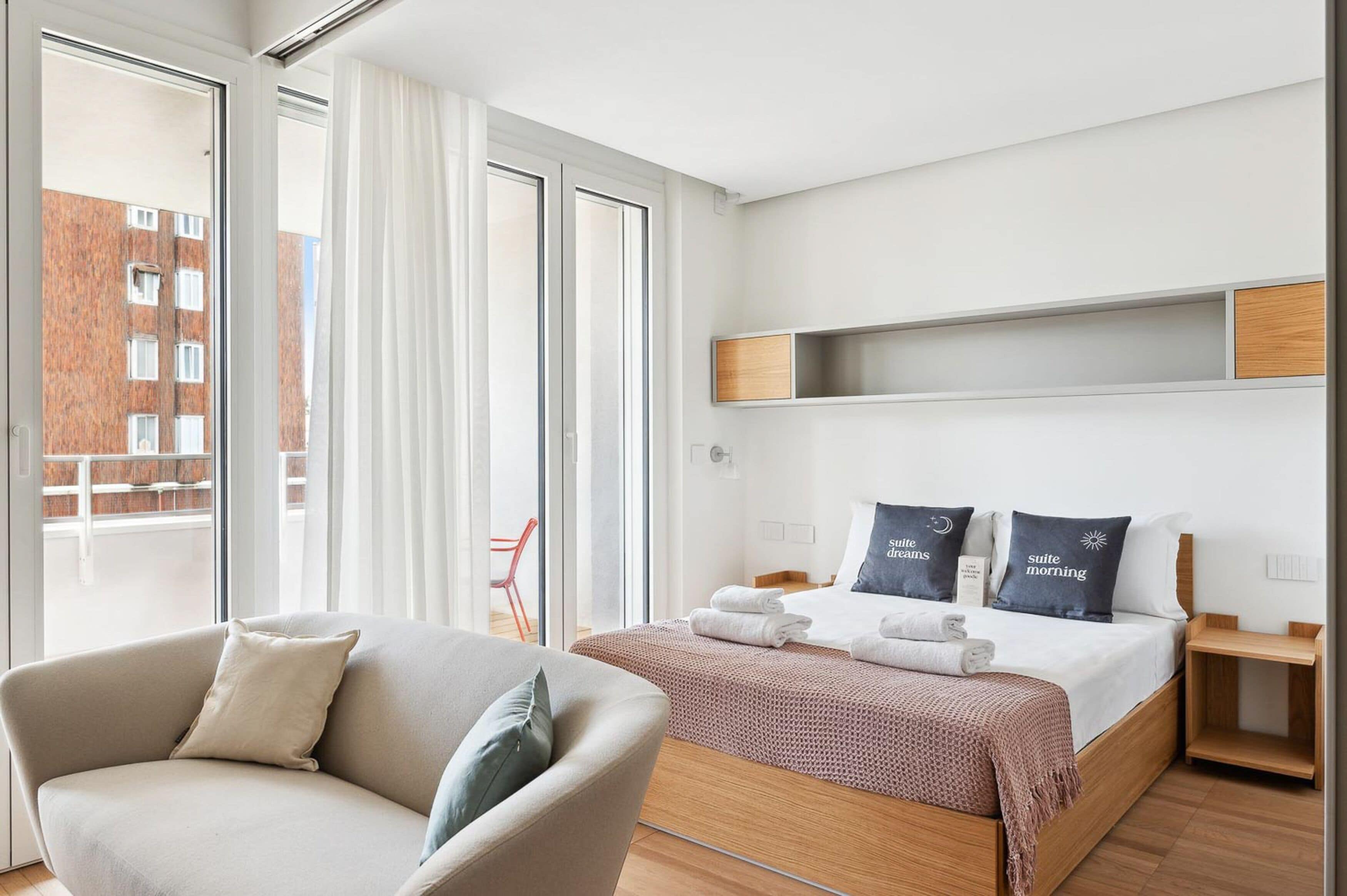 A modern hotel room with a bed, a sofa, and a large window with curtains.