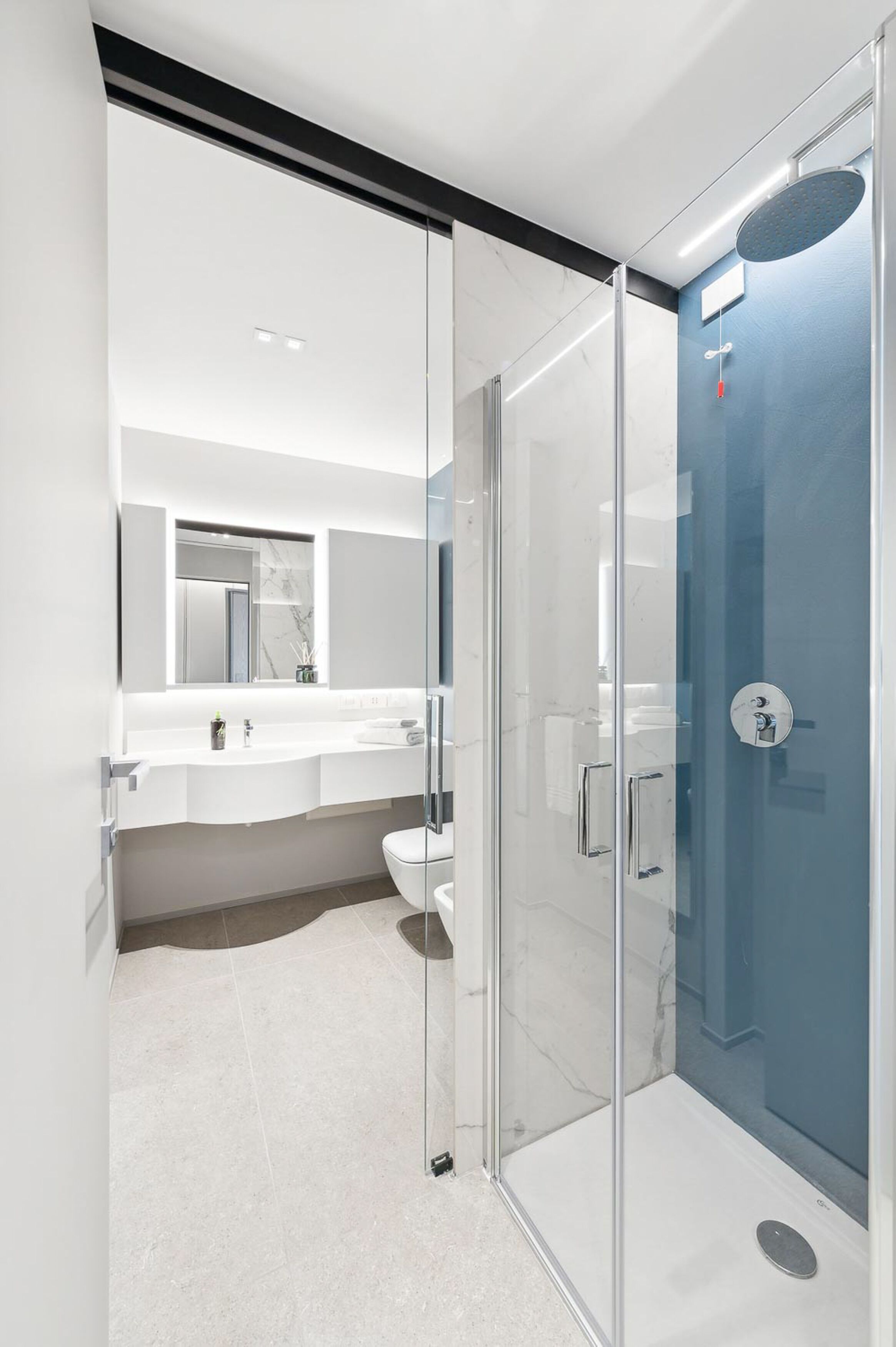 Un baño moderno con ducha envuelta en vidrio, lavamanos blanco y espejo grande.