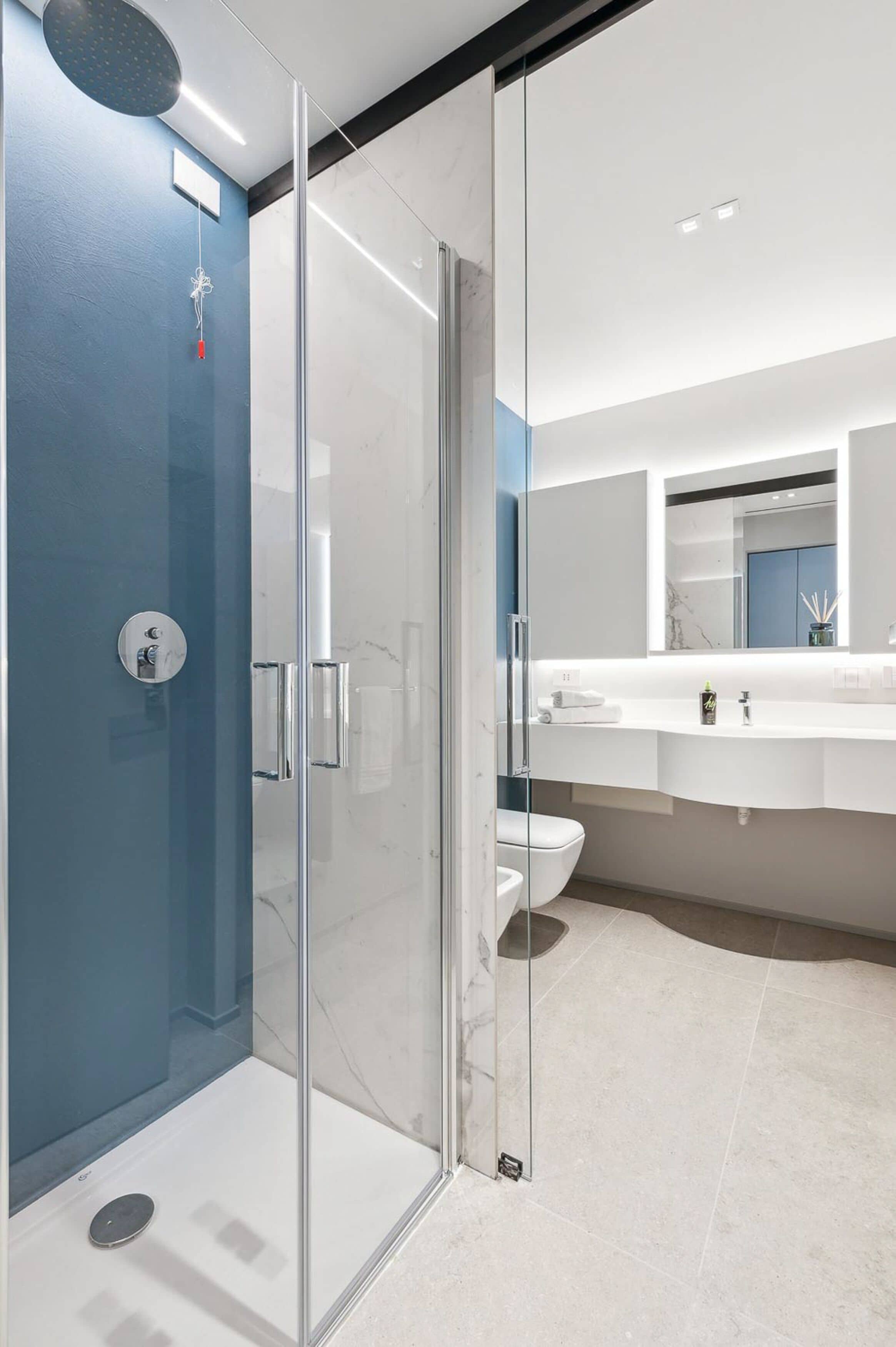 Une salle de bain moderne avec une douche à parois de verre, un lavabo blanc et un grand miroir.
