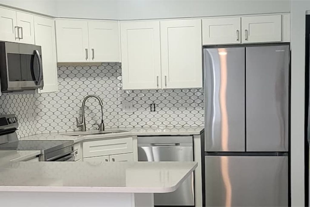 A modern kitchen with white cabinets, a stainless steel refrigerator, a microwave, and a dishwasher.