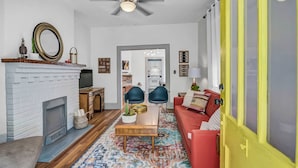 A living room with a white fireplace, a ceiling fan, a red sofa, and a colorful rug.