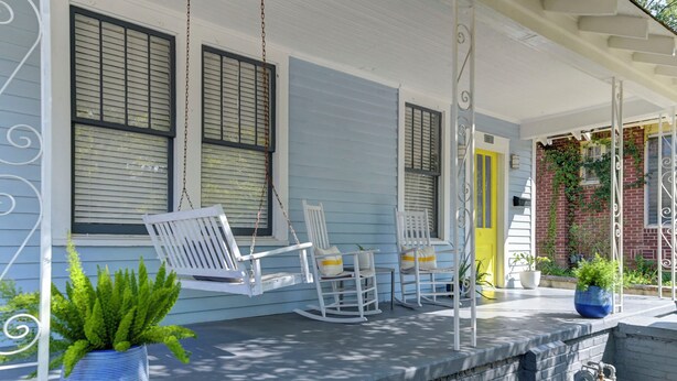 A porch with rocking chairs, a table, and potted plants.