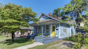 A single-story house with a front porch, a yellow door, and a brick pathway leading to the entrance.