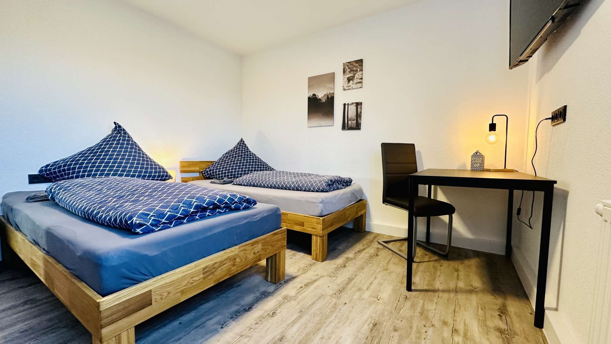 A small room with two wooden beds, a desk, and a chair.