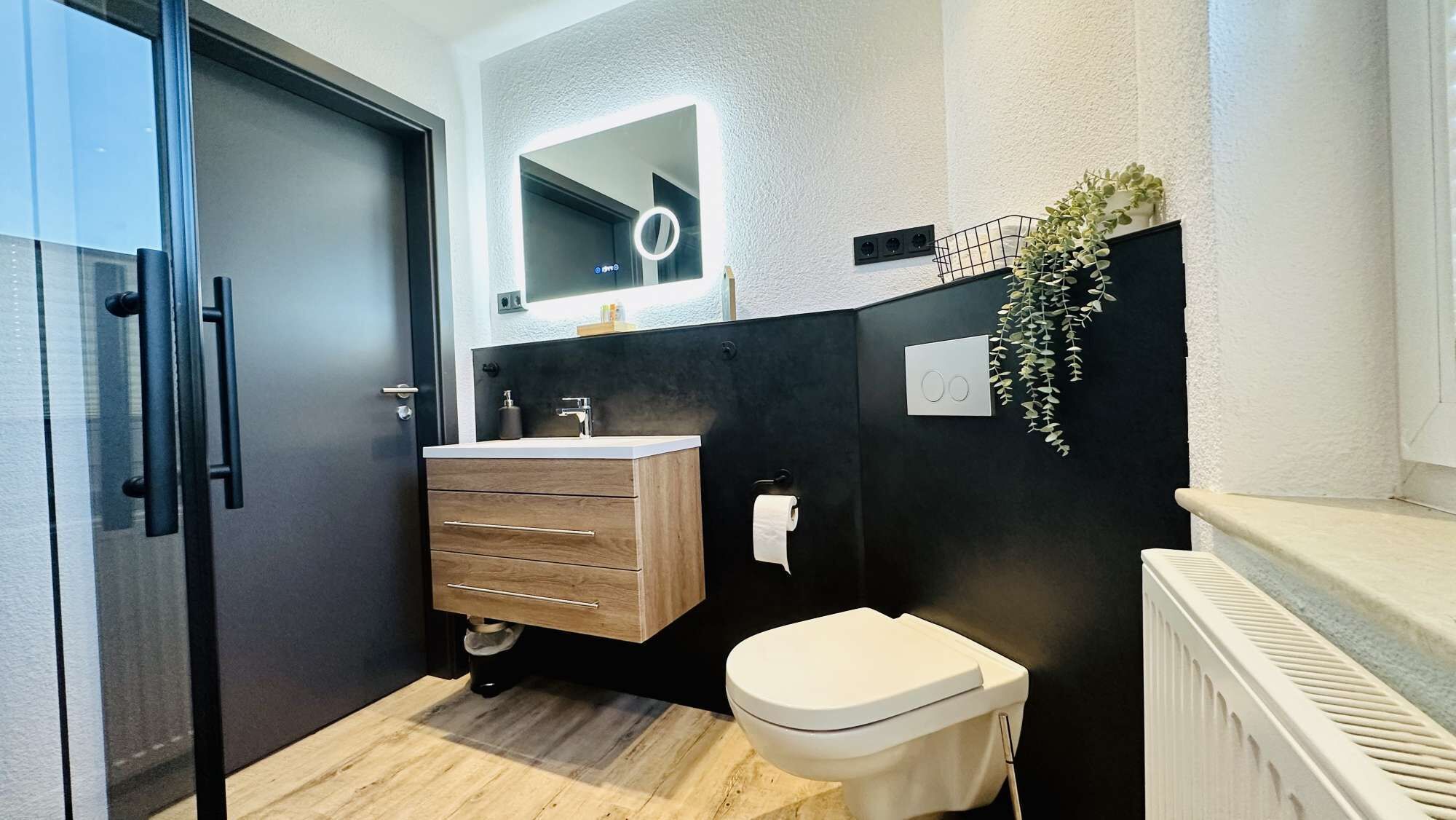 A modern bathroom with a wooden vanity, a toilet, and a mirror with a ring light.