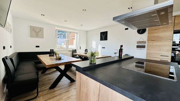 A modern kitchen with a wooden dining table, black chairs, and a black countertop. - B&W Apartments - 1. Etage Wohnung (Morschen)
