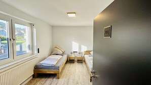 A small, bright room with two single beds, a small table, and a window with a view of the outside. - B&W Apartments - 1. Etage Wohnung (Morschen)