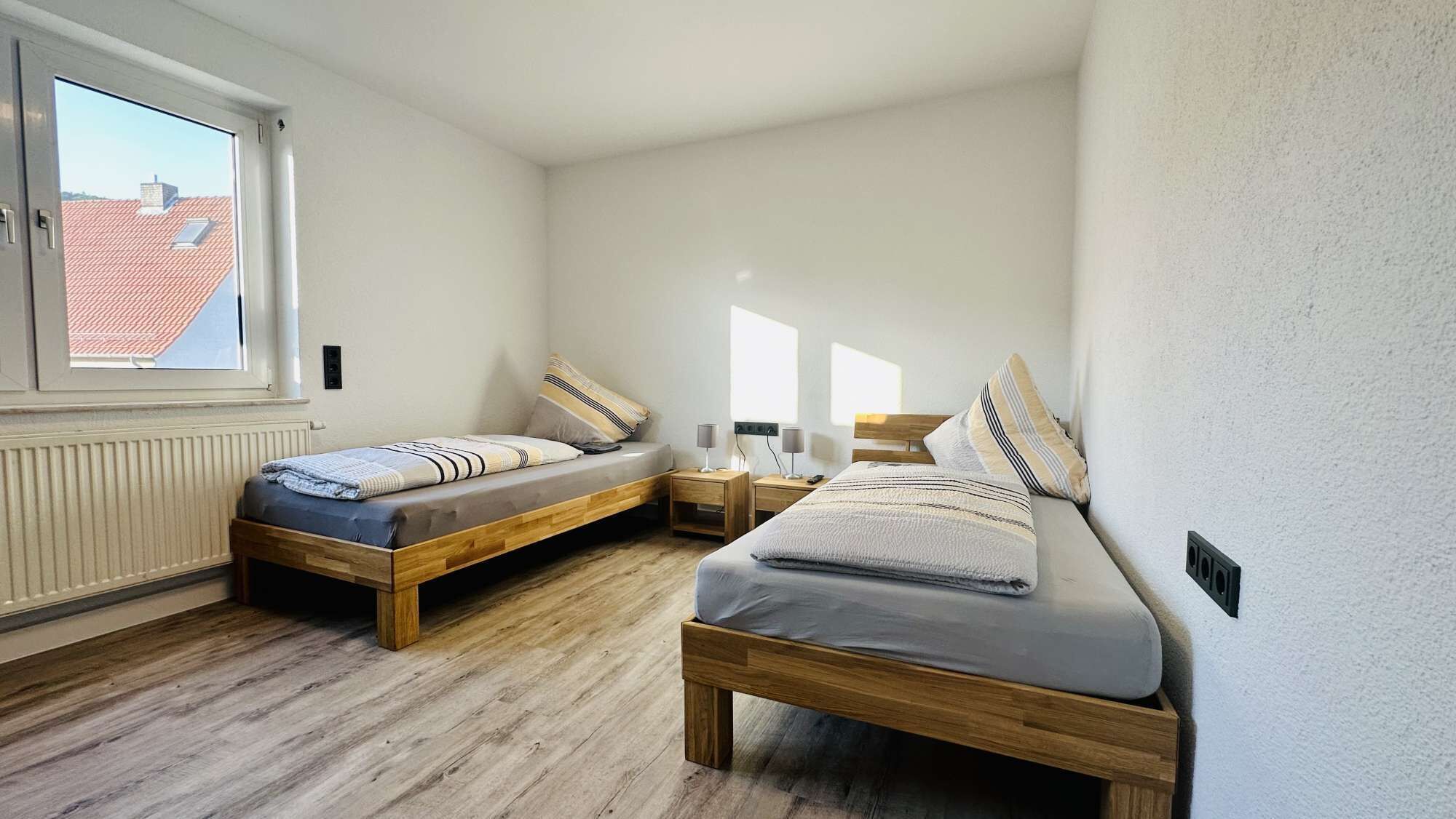 A bedroom with two wooden beds, a window, and a radiator.