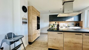 A modern kitchen with wooden cabinets, a black countertop, and a stainless steel range hood. - B&W Apartments - 1. Etage Wohnung (Morschen)