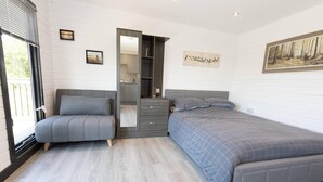 A bedroom with a grey sofa, a bed with grey bedding, a wardrobe, and a painting on the wall. - Beautiful Open Plan Lakeside Lodge, Shearsby (Lutterworth)