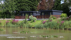 A modern house with a deck overlooking a pond with lily pads. - Beautiful Open Plan Lakeside Lodge, Shearsby (Lutterworth)